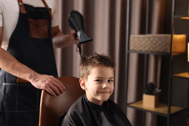 Photo of Professional barber blow drying boy's hair in barbershop, closeup