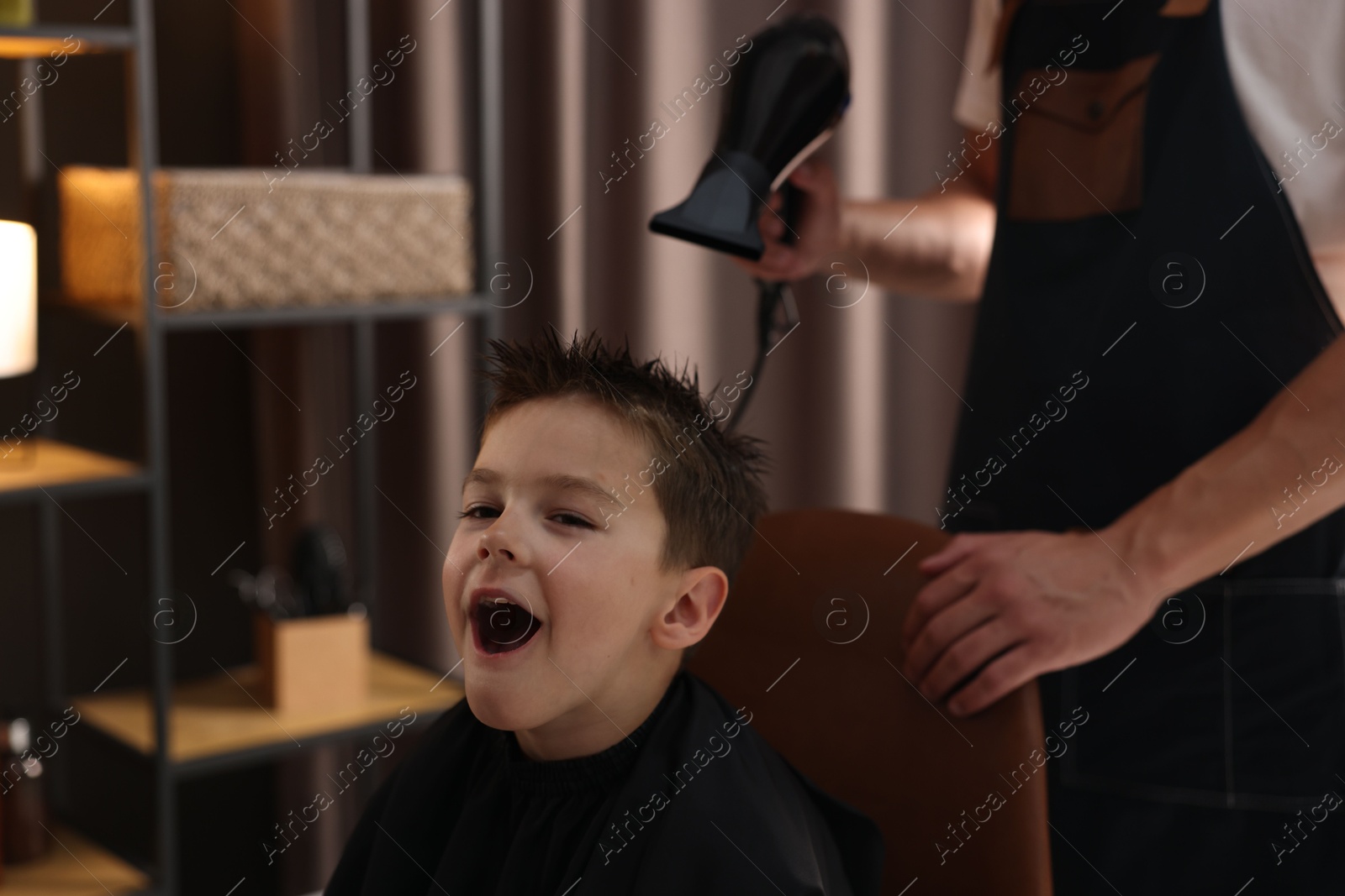 Photo of Professional barber blow drying boy's hair in barbershop, closeup