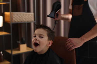 Photo of Professional barber blow drying boy's hair in barbershop, closeup
