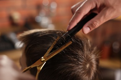 Photo of Professional barber cutting boy's hair in barbershop, closeup
