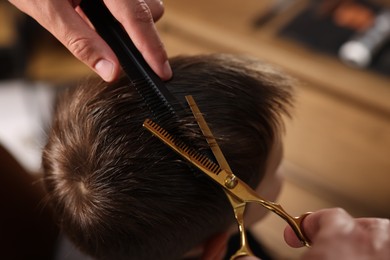 Photo of Professional barber cutting boy's hair in barbershop, closeup