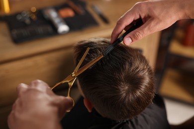 Photo of Professional barber cutting boy's hair in barbershop, above view