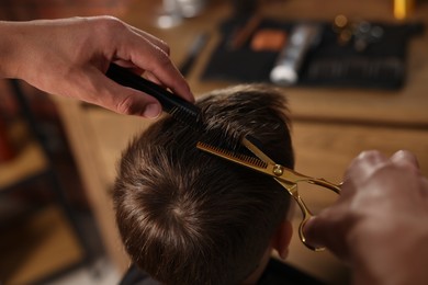 Photo of Professional barber cutting boy's hair in barbershop, above view