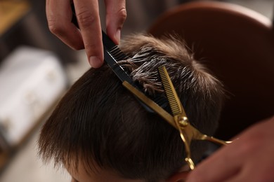 Photo of Professional barber cutting boy's hair in barbershop, closeup