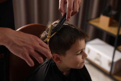 Photo of Professional barber cutting boy's hair in barbershop, closeup