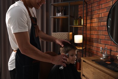 Photo of Professional barber working with little boy in barbershop, closeup