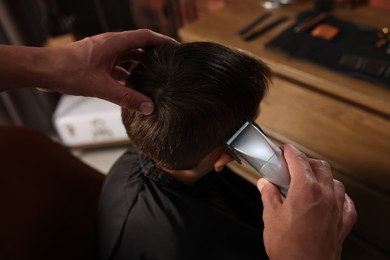 Photo of Professional barber working with little boy in barbershop, above view