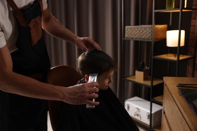 Photo of Professional barber working with little boy in barbershop, closeup