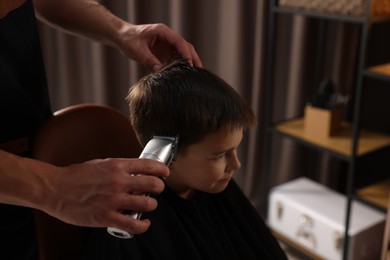 Photo of Professional barber working with little boy in barbershop, closeup