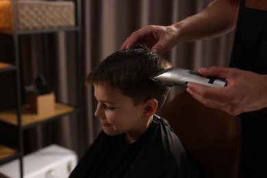 Photo of Professional barber working with little boy in barbershop, closeup
