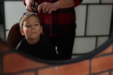 Photo of Professional barber working with little boy in barbershop, closeup