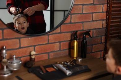Photo of Professional barber working with little boy in barbershop, closeup