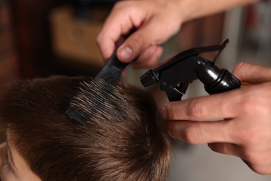 Photo of Professional barber working with little boy in barbershop, closeup