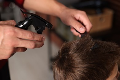 Photo of Professional barber working with little boy in barbershop, closeup