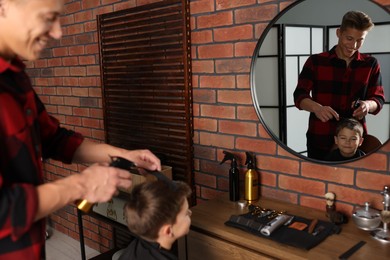 Photo of Professional barber working with little boy in barbershop