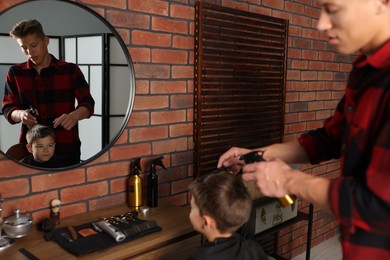 Photo of Professional barber working with little boy in barbershop