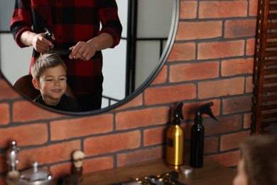 Photo of Professional barber working with little boy in barbershop, closeup