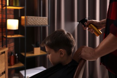 Photo of Professional barber working with little boy in barbershop, closeup