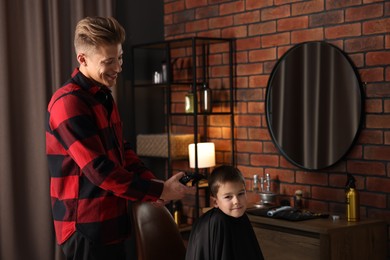 Photo of Professional barber working with little boy in barbershop