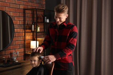 Photo of Professional barber working with little boy in barbershop