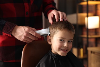 Photo of Professional barber working with little boy in barbershop, closeup