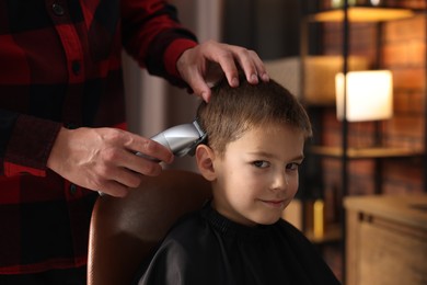 Photo of Professional barber working with little boy in barbershop, closeup