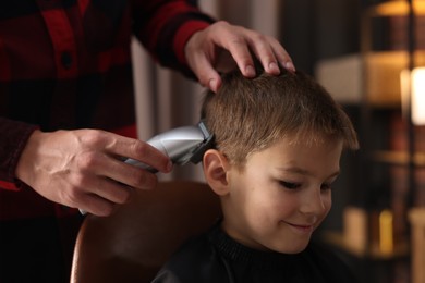 Photo of Professional barber working with little boy in barbershop, closeup