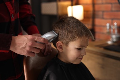 Photo of Professional barber working with little boy in barbershop, closeup