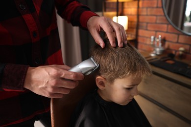 Photo of Professional barber working with little boy in barbershop, closeup