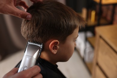 Photo of Professional barber working with little boy in barbershop, closeup