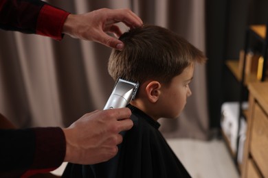 Photo of Professional barber working with little boy in barbershop, closeup