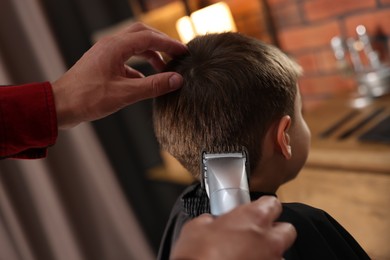 Photo of Professional barber working with little boy in barbershop, closeup