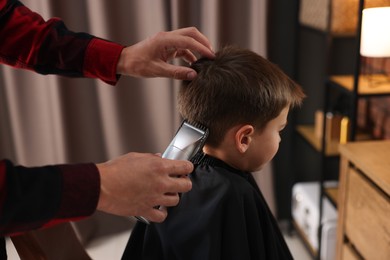 Photo of Professional barber working with little boy in barbershop, closeup