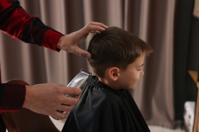 Photo of Professional barber working with little boy in barbershop, closeup