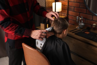 Photo of Professional barber working with little boy in barbershop, closeup