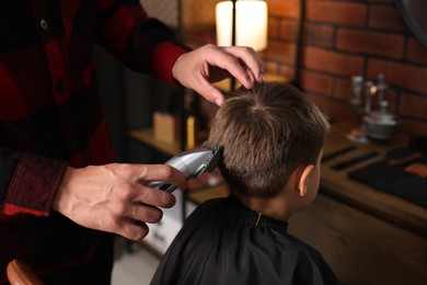 Photo of Professional barber working with little boy in barbershop, closeup