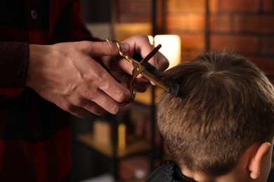 Photo of Professional barber cutting boy's hair in barbershop, closeup