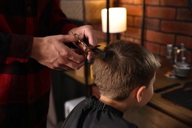Photo of Professional barber cutting boy's hair in barbershop, closeup