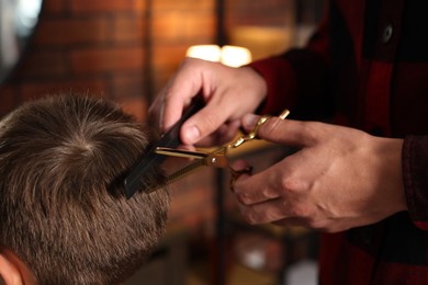 Photo of Professional barber cutting boy's hair in barbershop, closeup