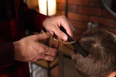 Photo of Professional barber cutting boy's hair in barbershop, closeup