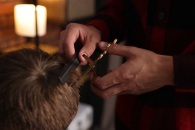Photo of Professional barber cutting boy's hair in barbershop, closeup