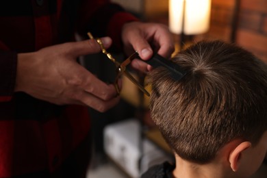 Photo of Professional barber cutting boy's hair in barbershop, closeup