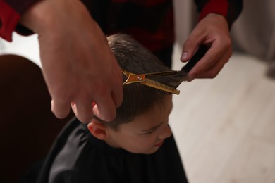 Photo of Professional barber cutting boy's hair in barbershop, above view