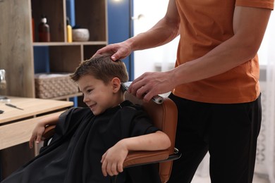Photo of Professional barber working with little boy in barbershop, closeup
