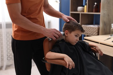 Photo of Professional barber working with little boy in barbershop, closeup