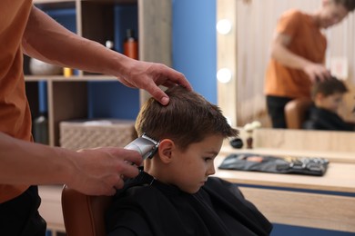 Photo of Professional barber working with little boy in barbershop, closeup