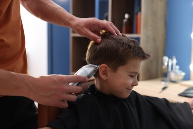 Photo of Professional barber working with little boy in barbershop, closeup