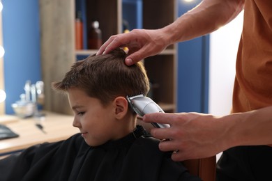 Photo of Professional barber working with little boy in barbershop, closeup