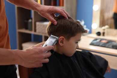 Photo of Professional barber working with little boy in barbershop, closeup