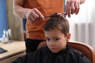 Photo of Professional barber cutting boy's hair in barbershop, closeup